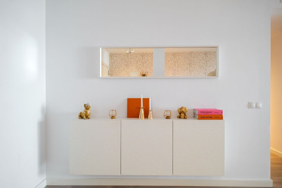 Modern white cabinet with decorative items including dog figurines, books, and candleholders. A mirror with patterned wallpaper is above.