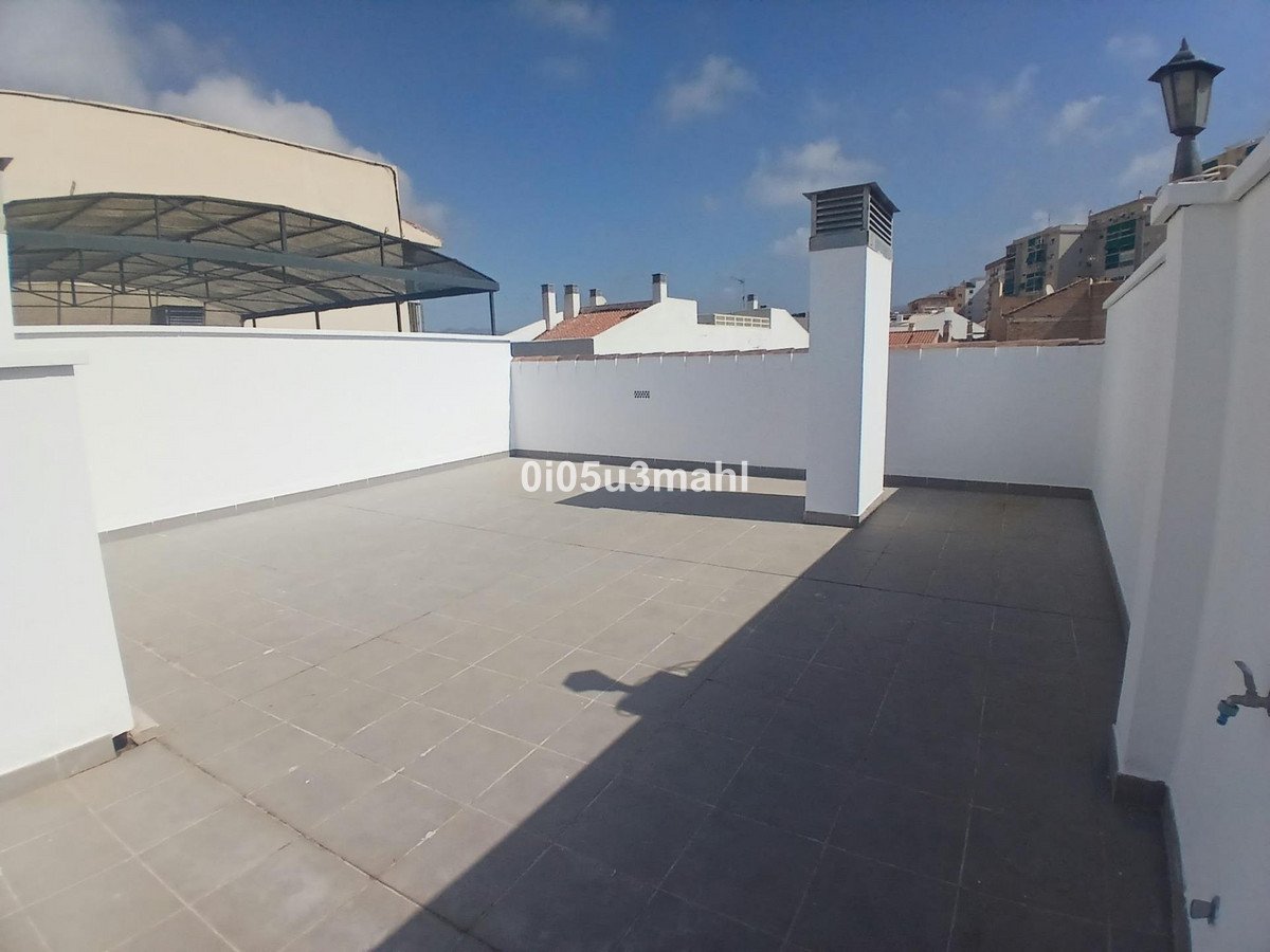 Spacious tiled terrace with white walls, a chimney, a lamppost, and a view of buildings.