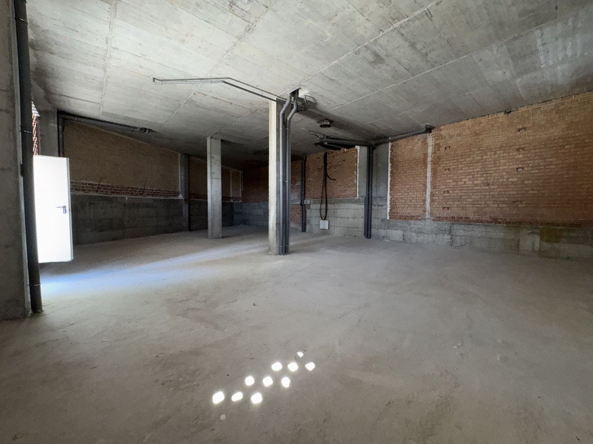 Unfinished commercial space with exposed brick walls, concrete floors and ceiling, and overhead lighting fixtures.