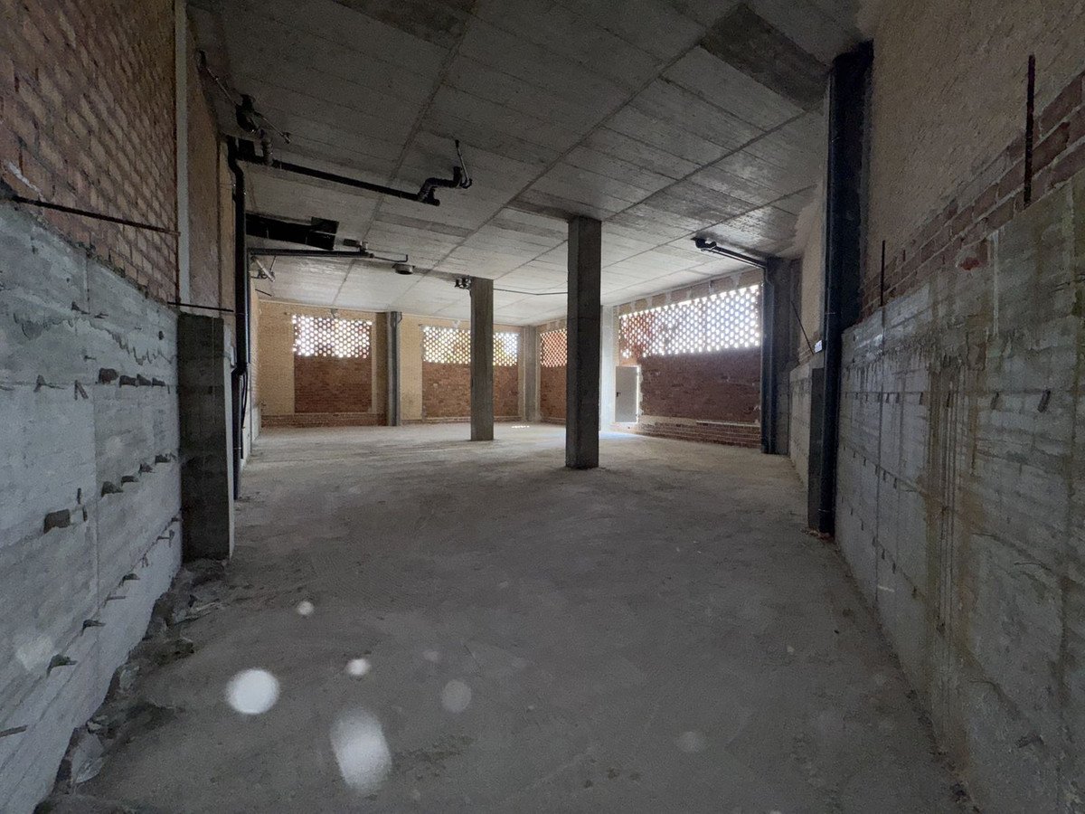 Unfinished commercial space with concrete floors and brick walls, featuring columns and patterned windows.