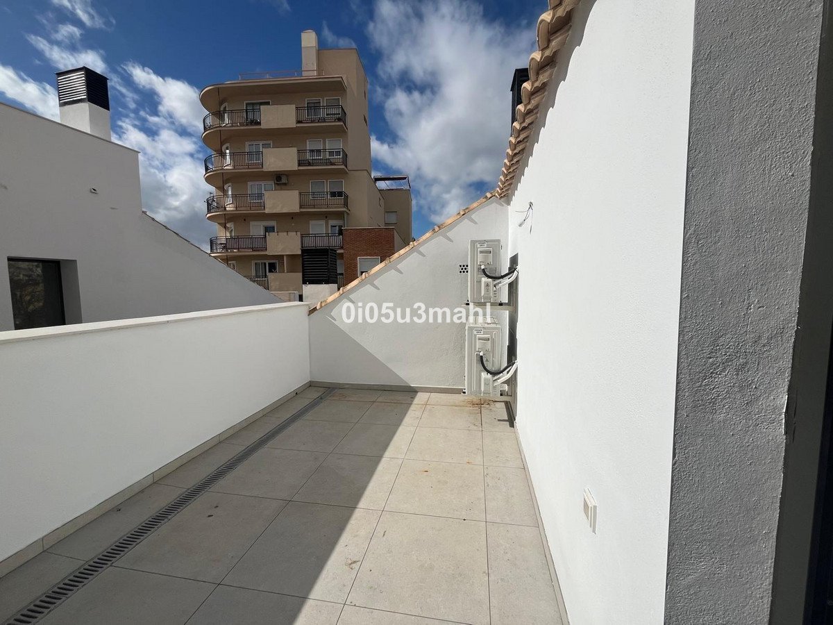 A spacious terrace with tiled flooring and white walls, offering views of a modern building and a blue sky with clouds.