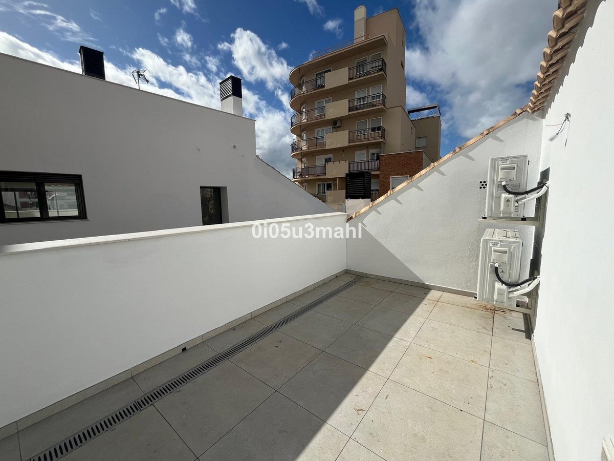 A spacious terrace with tiled flooring, white walls, and views of buildings under a cloudy blue sky.