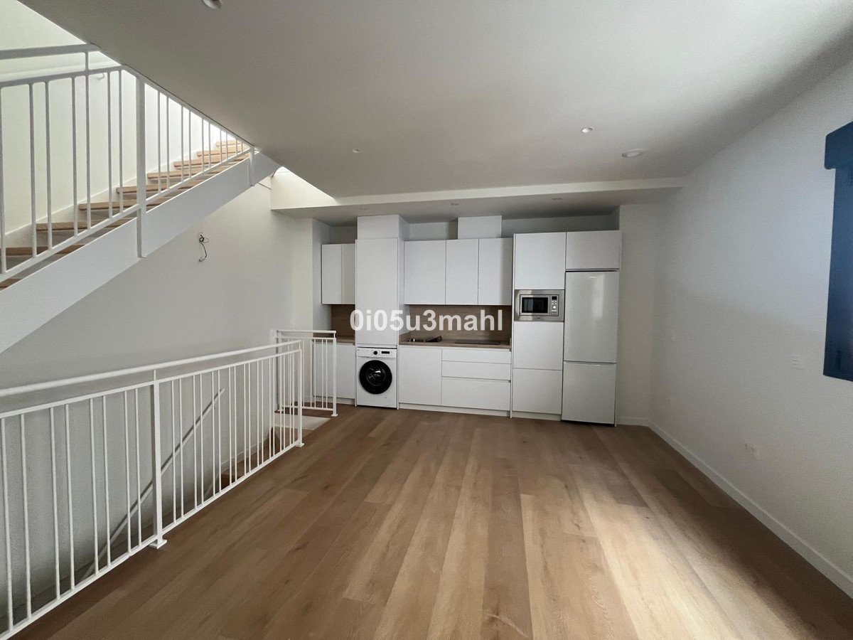 Modern white kitchen with integrated appliances, a washing machine, and wooden floors, adjacent to a white staircase.