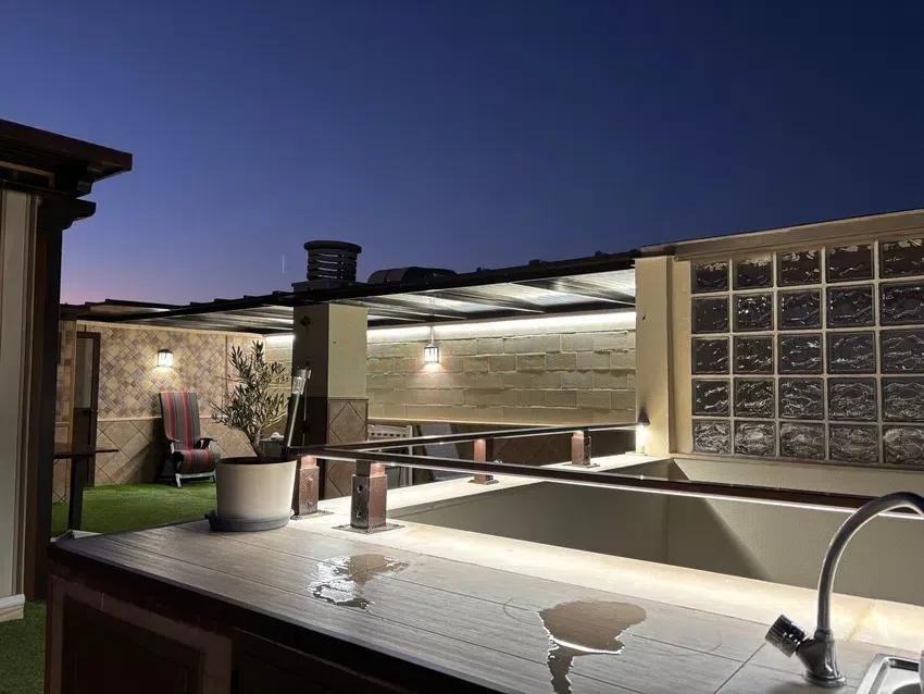 Rooftop patio at dusk with an outdoor kitchen counter, seating area, and modern lighting.