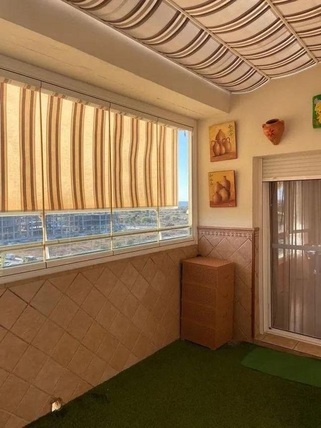 Sunroom with striped blinds, wicker cabinet, and view of buildings and the sea beyond.