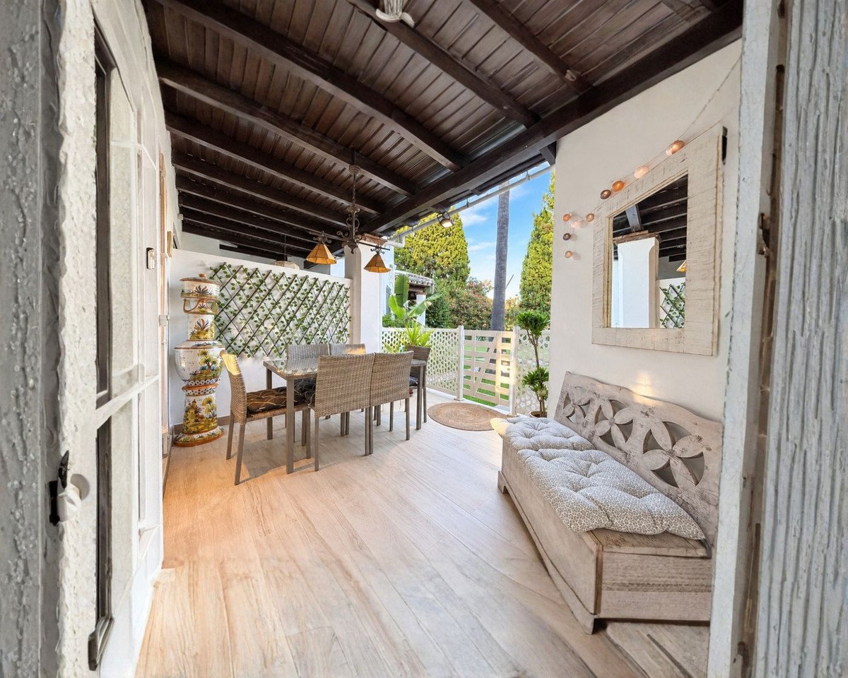 Covered terrace with dining table and chairs, a wooden bench, and decorative elements. Lush greenery visible in the background.