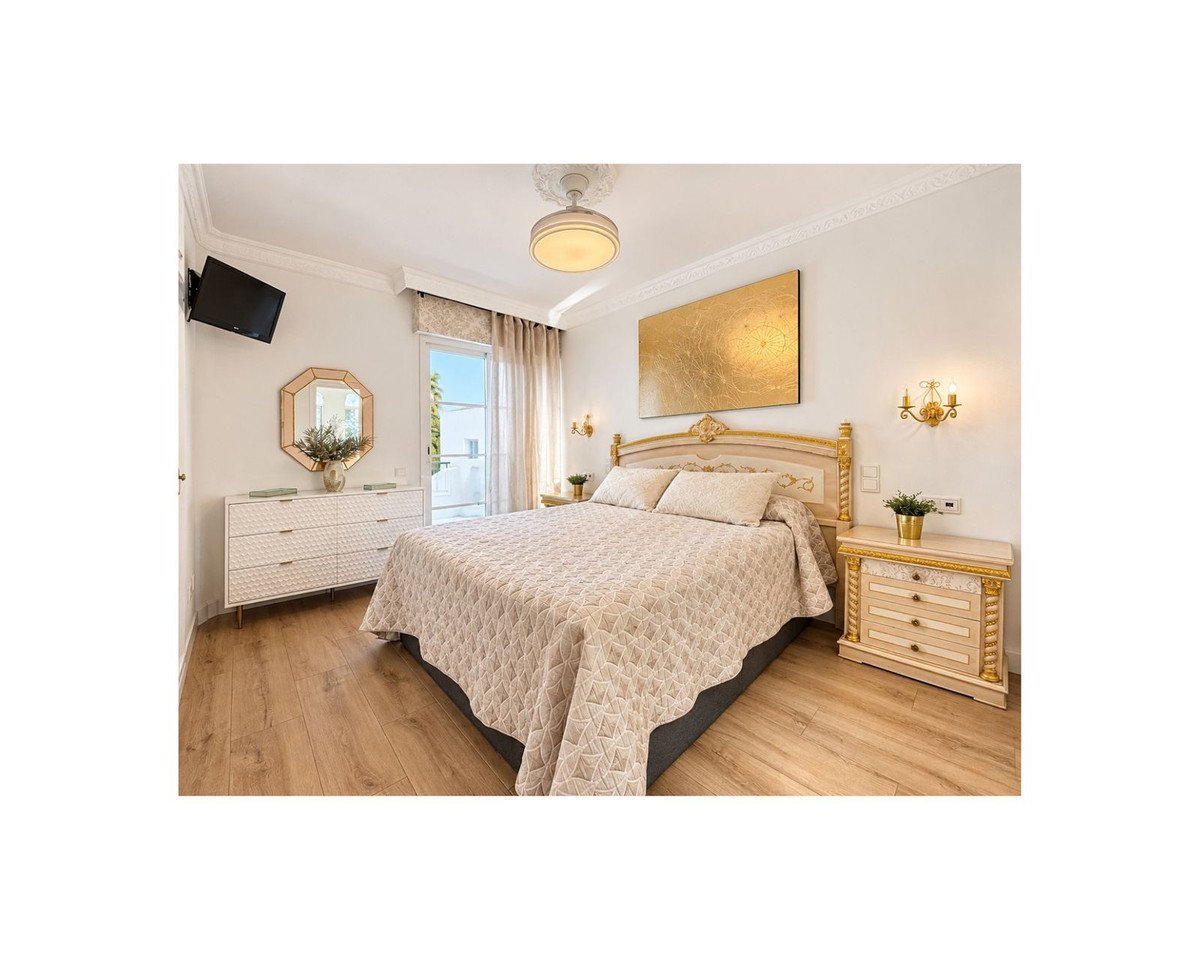 A luxurious bedroom featuring a large bed, elegant furniture, a wall-mounted TV, and a balcony with a view.