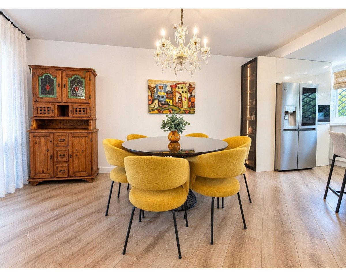 Modern dining area with yellow chairs around a round table, adjacent to a sleek kitchen with stainless steel appliances.