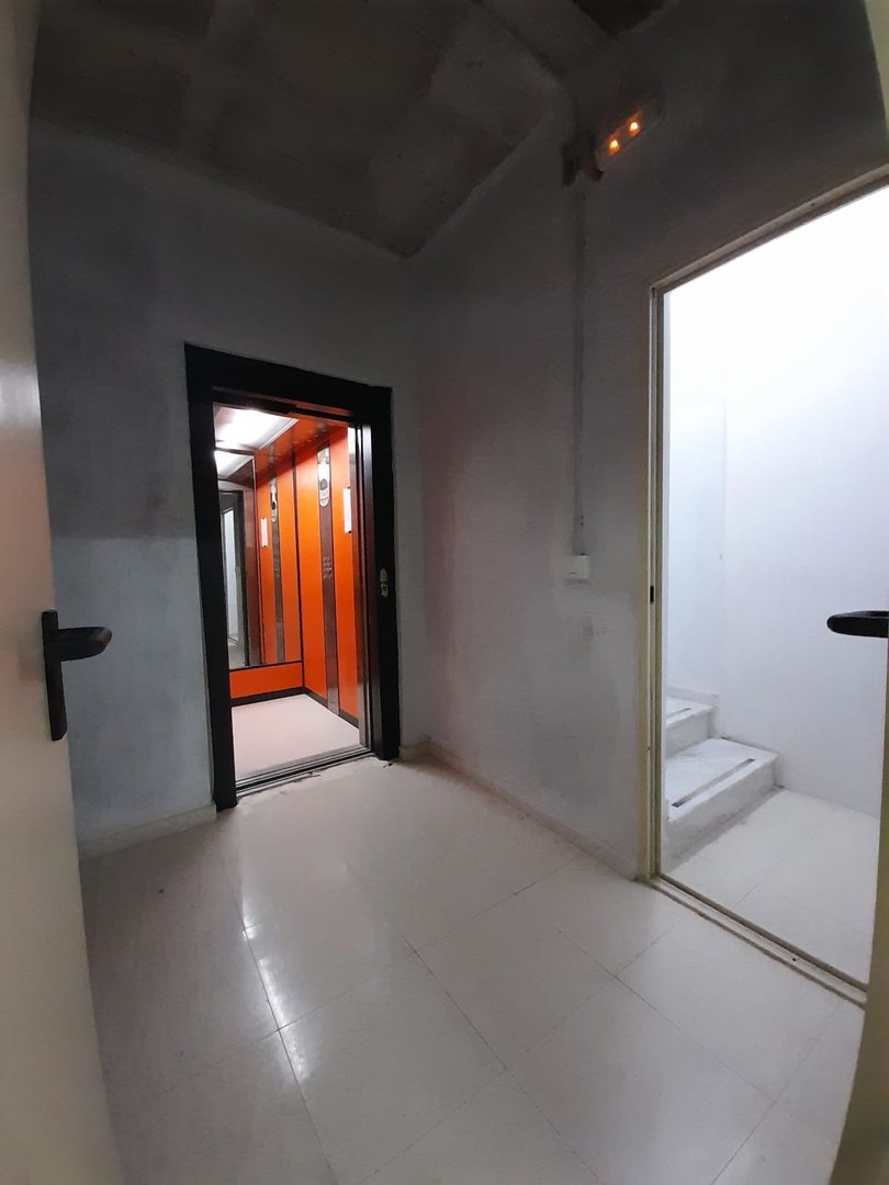 Empty hallway with white walls and an orange elevator