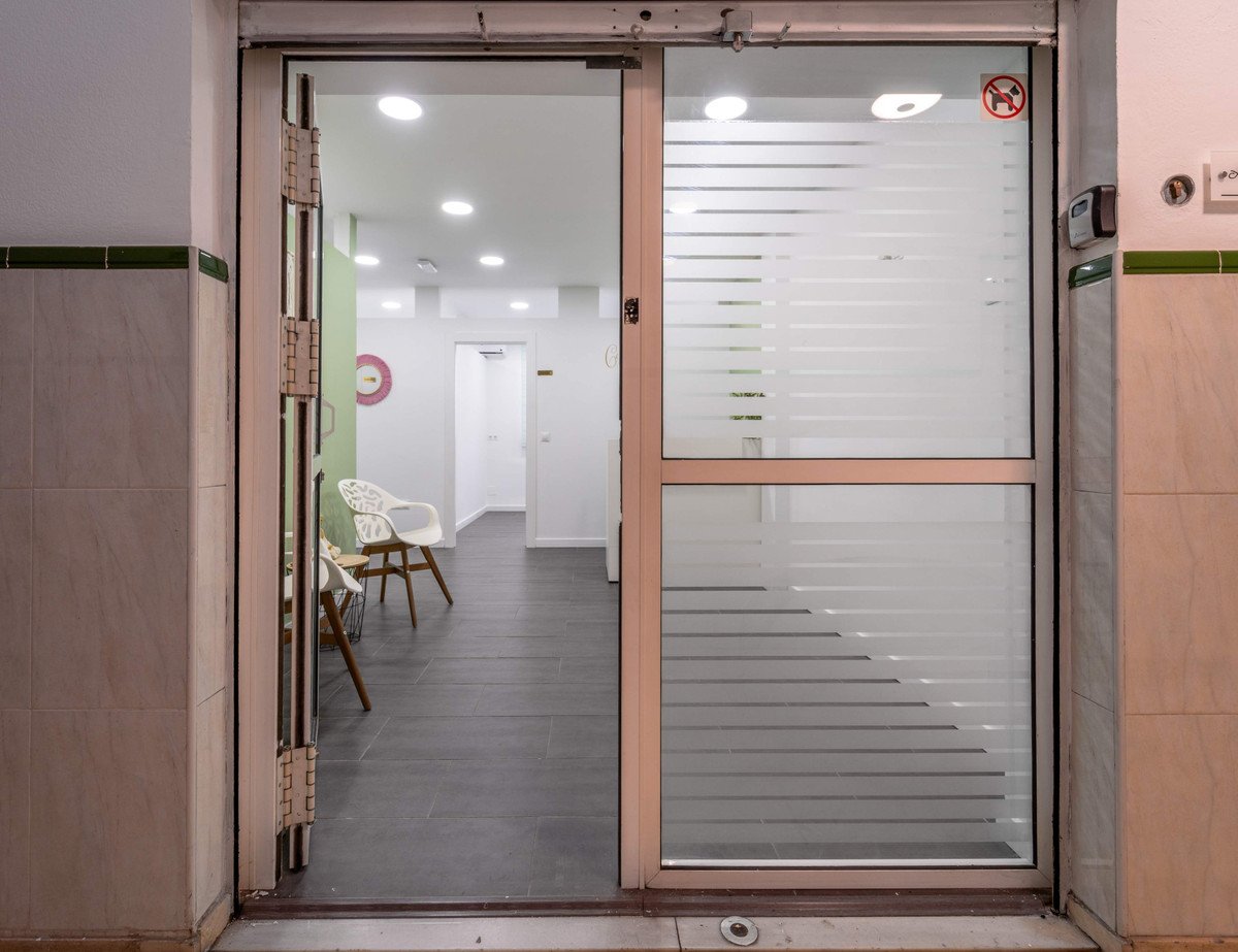 Interior view of a modern office space with glass door, white chairs, and tiled walls.