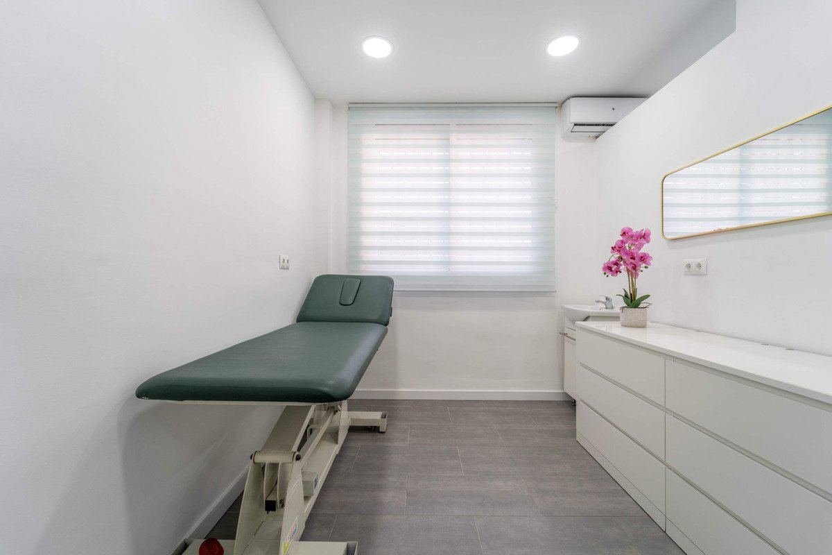 A clean, modern medical examination room with a window, cabinets, and a green examination table.
