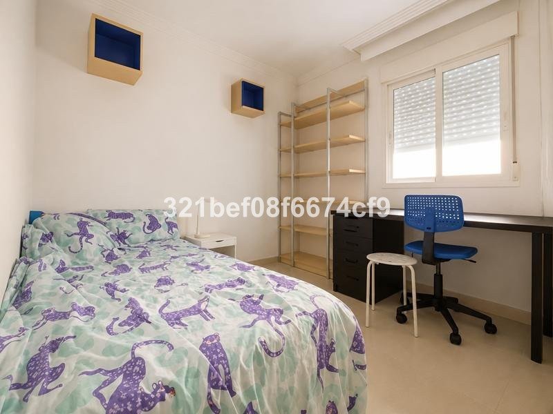 A bedroom featuring a bed with unique patterned bedding, a desk with a blue chair, and open shelving units.