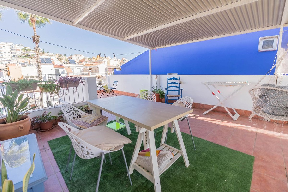 A covered terrace with a dining table and chairs, artificial turf, and a view of a town with blue and white buildings.