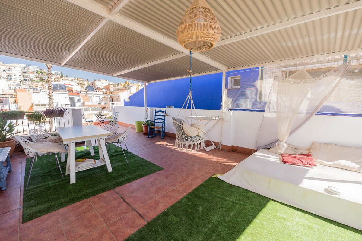 A rooftop terrace with a dining table, hanging chair, and a large daybed, overlooking a town with blue walls painted blue.