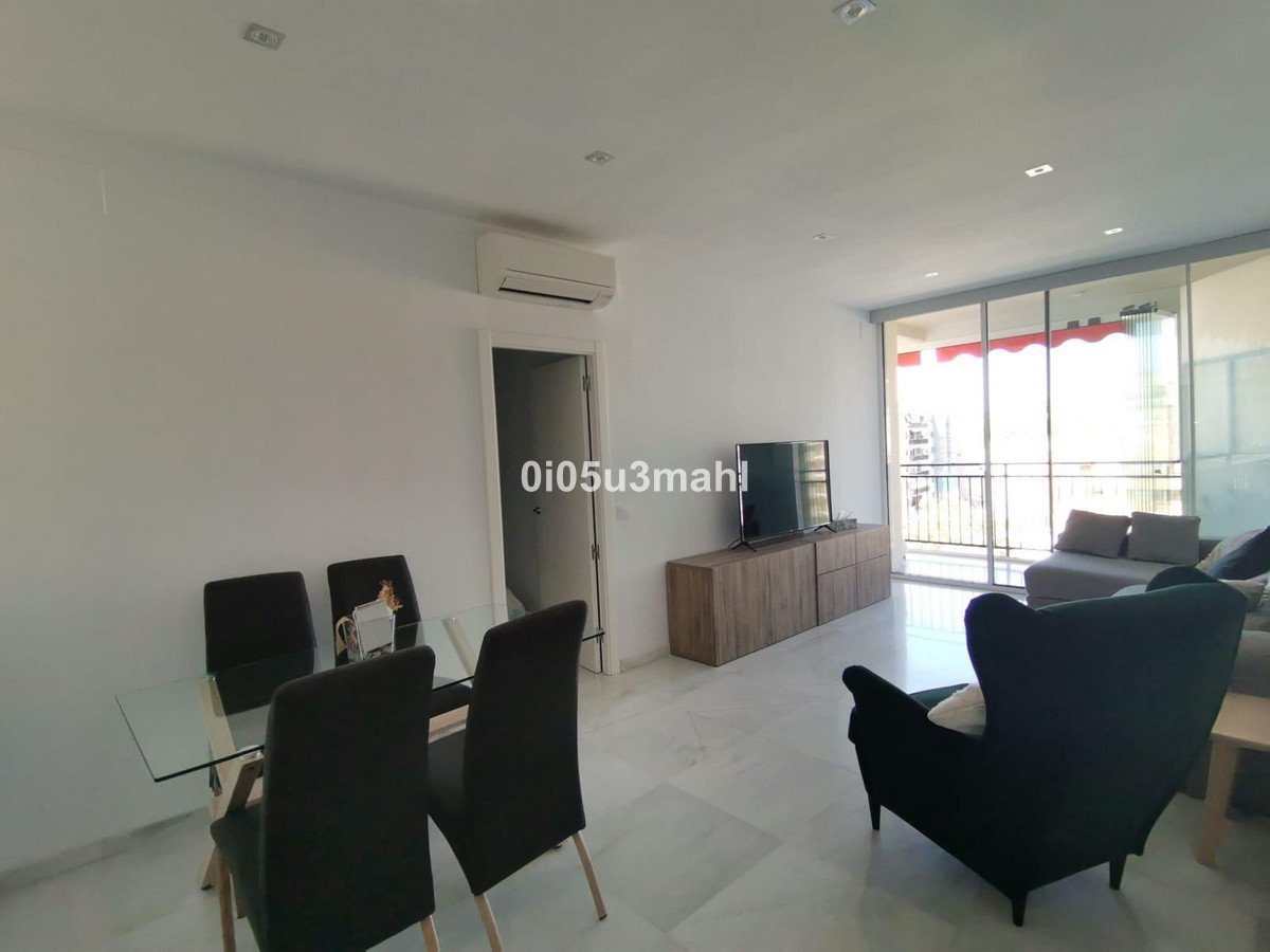 Modern living room with glass dining table, black chairs, TV, and balcony view.