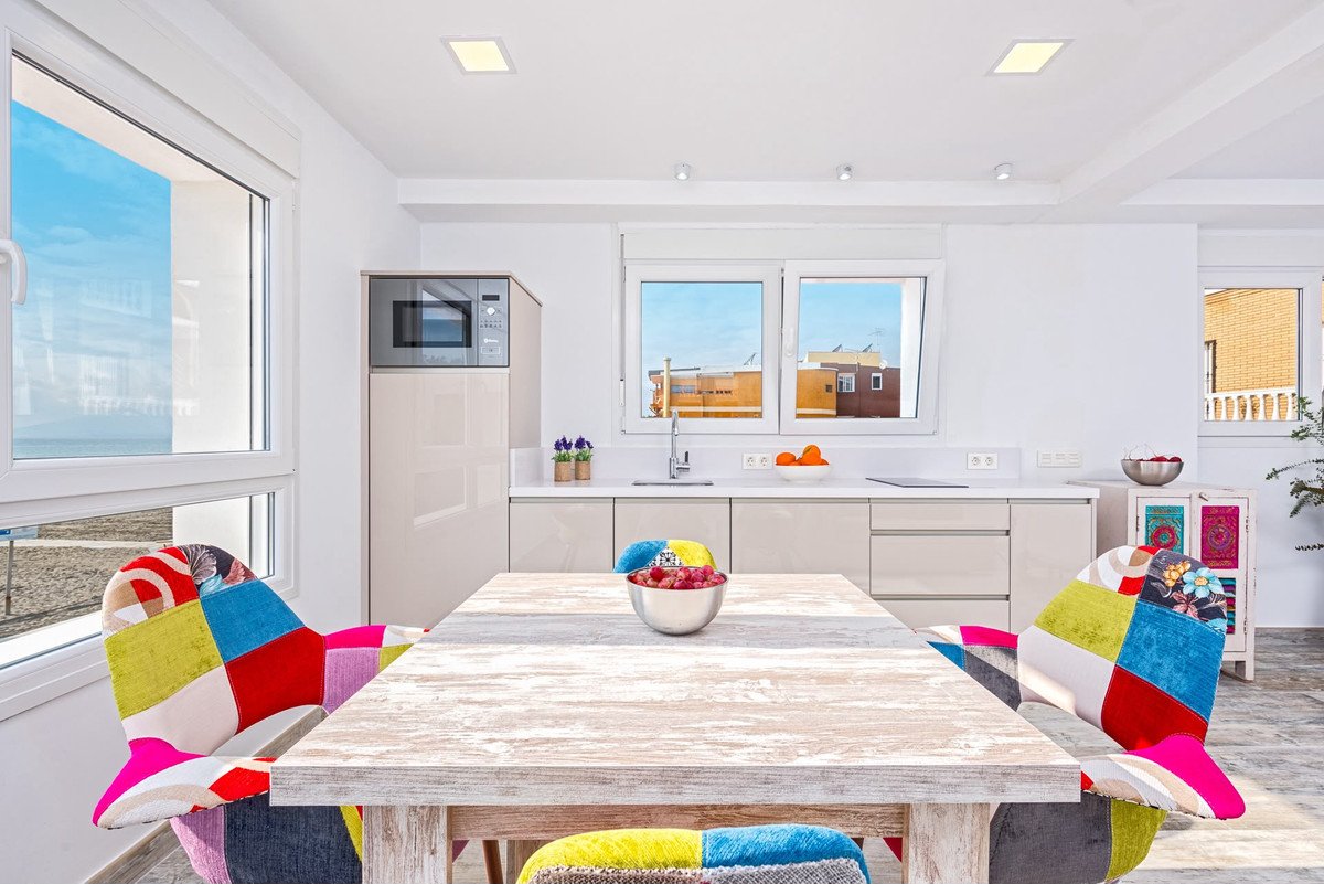 Modern kitchen and dining area with colorful chairs, a microwave, and views of the sea and buildings through the windows.