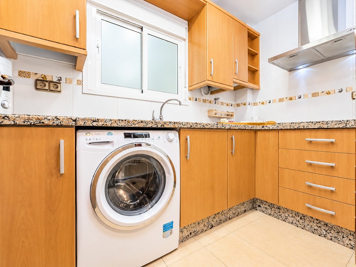 Modern kitchen with wood cabinets, a washing machine, granite countertops, and a window.
