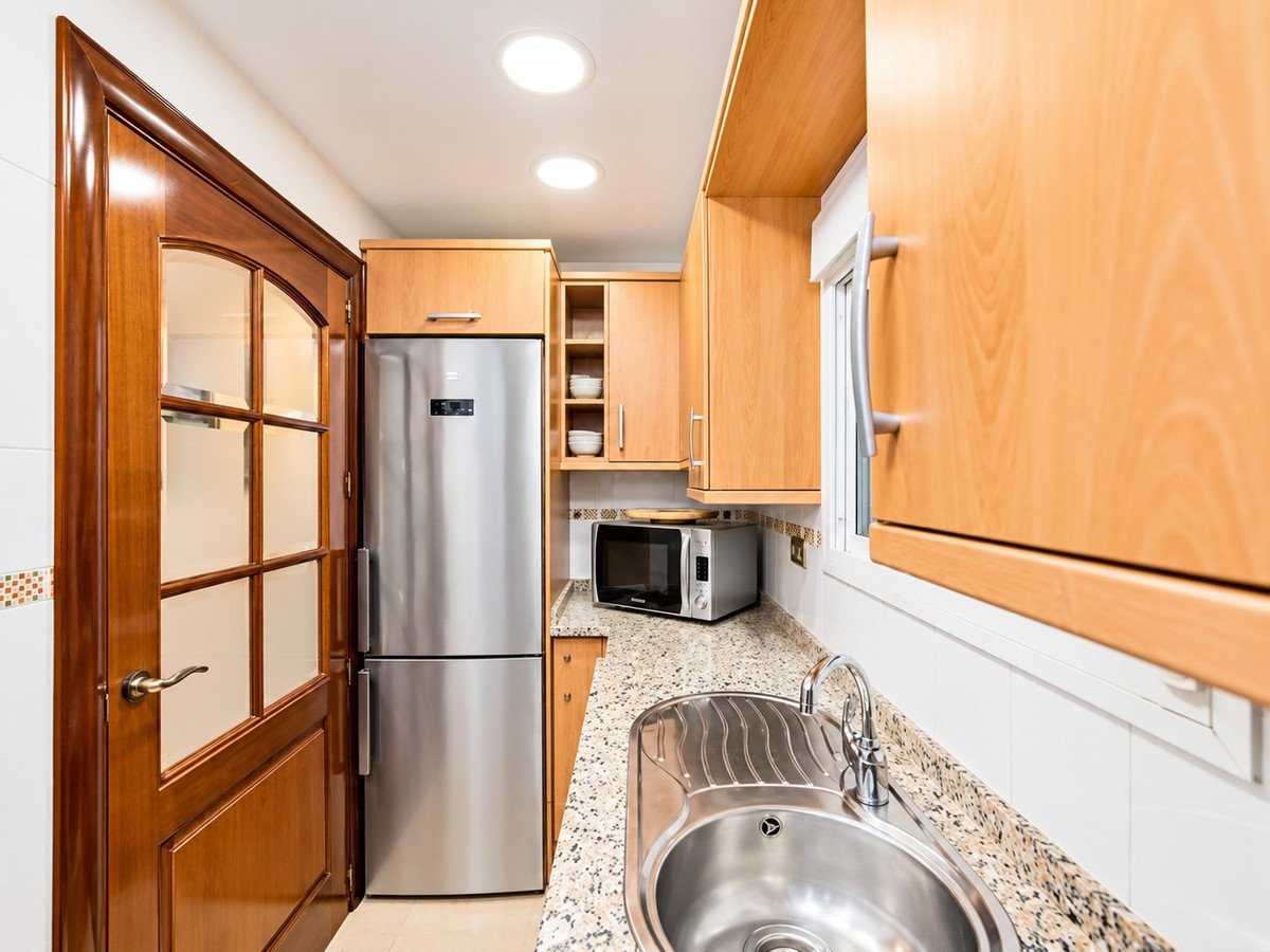 Modern kitchen with stainless steel refrigerator, microwave, sink, and light wood cabinets.