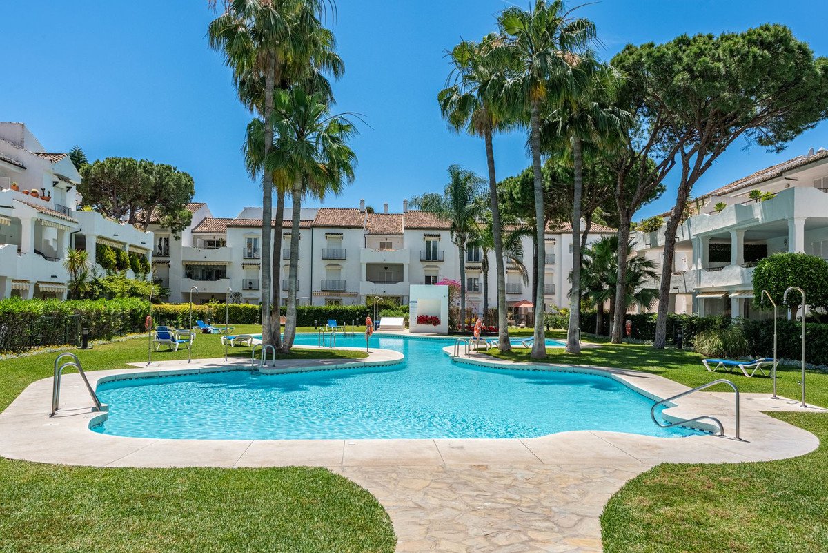 Villa with pool, palm trees, and green lawn under clear blue sky.
