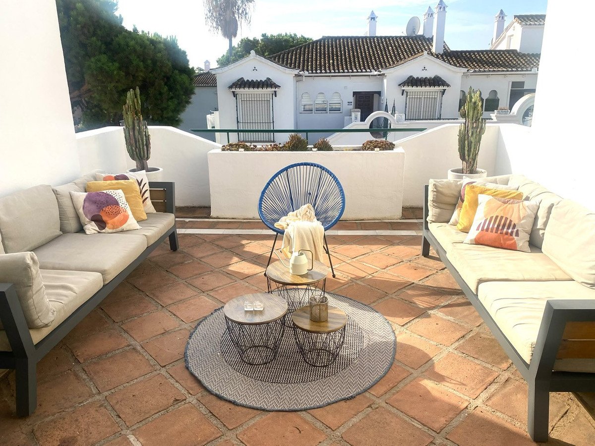 Terrace seating area with two sofas, colorful cushions, coffee tables, round rug, blue chair, and cacti.