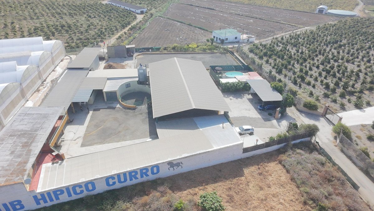 Aerial view of an equestrian center with greenhouses, riding arena, pool, and surrounding fields.