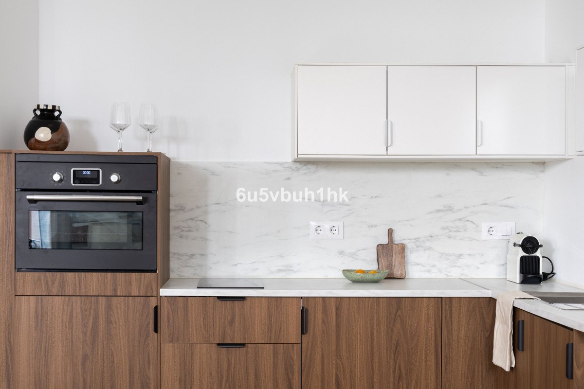 Modern kitchen featuring a built-in oven, white cabinets, marble backsplash, and wooden lower cabinets.