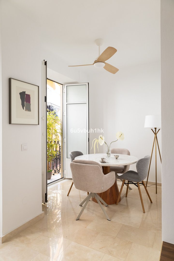Bright dining area with a round table, chairs, a ceiling fan, and an open balcony door with greenery view.
