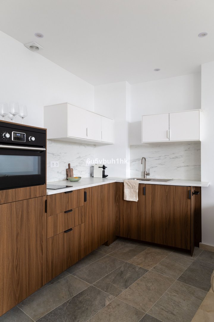 A modern kitchen with sleek wooden cabinets, white countertops, built-in oven, and a marble backsplash.