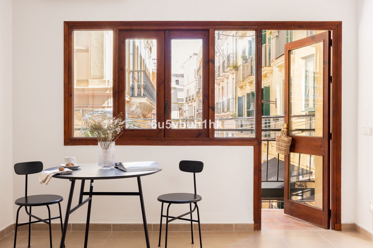 A small dining area with two chairs and a table, featuring a large wooden window and a balcony door with a view of a city street.