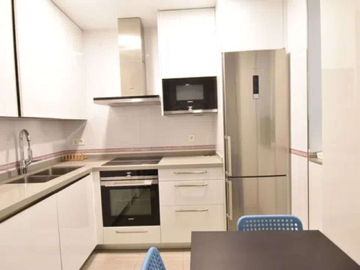 Modern kitchen with stainless steel appliances, including a refrigerator, oven, microwave, and sink, with white cabinetry.