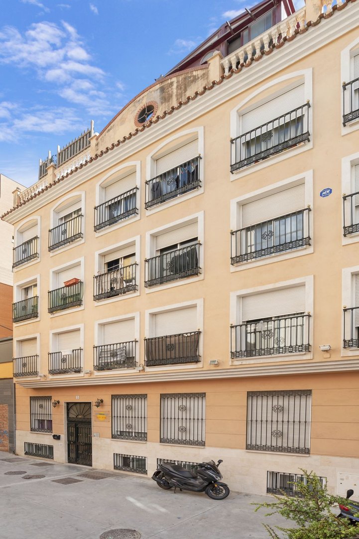 Exterior view of a pale yellow apartment building with multiple balconies, window shutters, and a scooter parked outside.