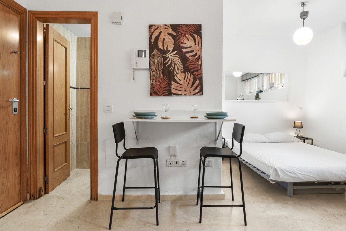 Studio apartment with a dining area for two, a bed, and an open doorway revealing a tiled bathroom.