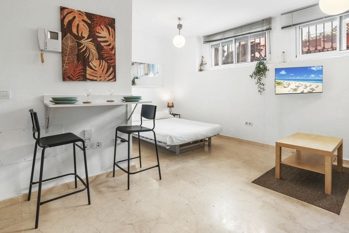 Compact studio apartment with a bed, fold-down dining table with stools, and a small coffee table.