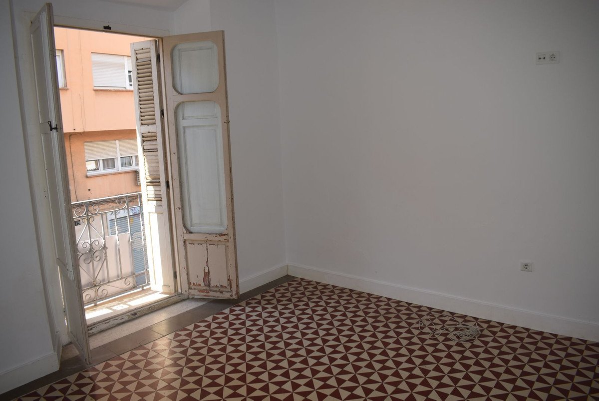 An empty room with a distinctive geometric tiled floor and an open door leading to a small balcony overlooking a building facade.