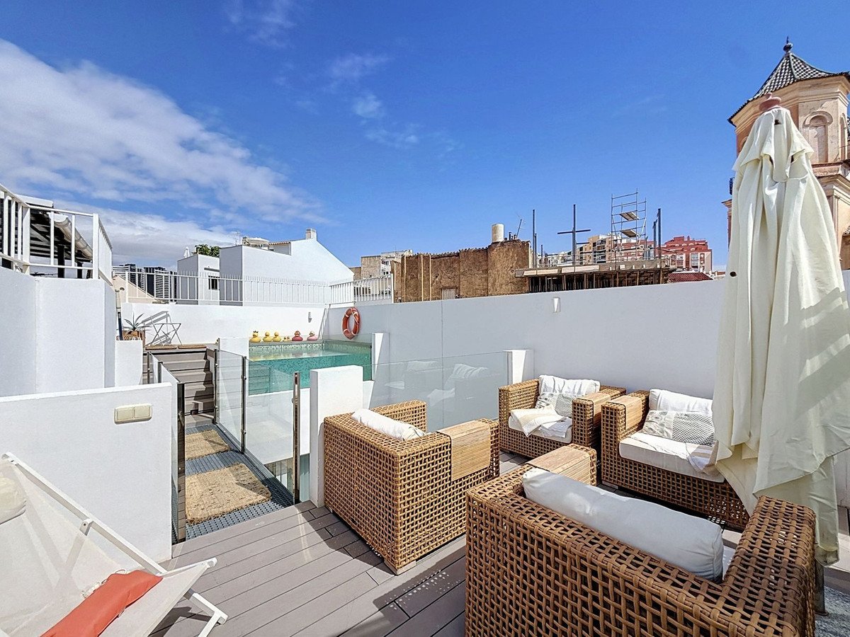 A rooftop terrace with a swimming pool, lounge seating, and white outdoor furniture, offering a view of the cityscape under a blue sky.