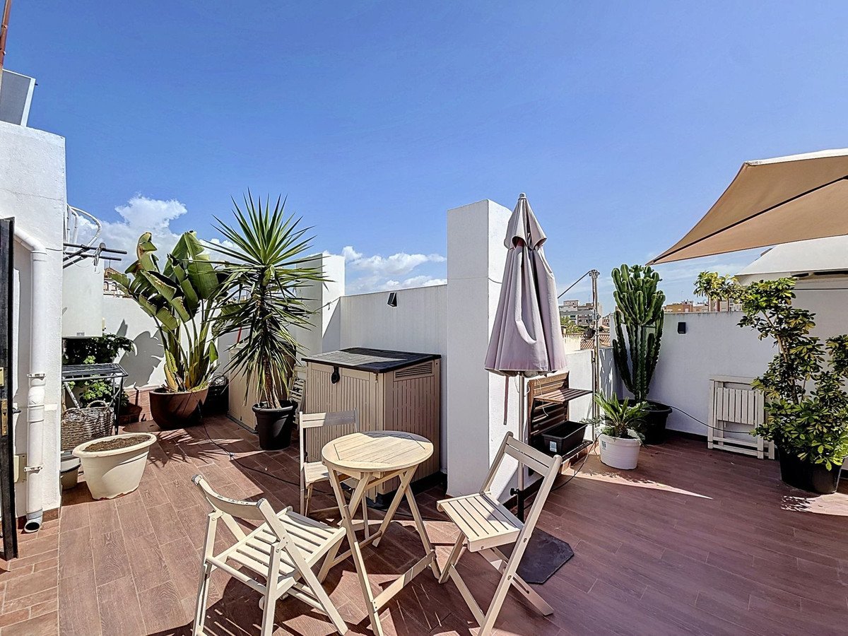 Terrace with wooden flooring, table, chairs, plants, and umbrellas under a clear blue sky.