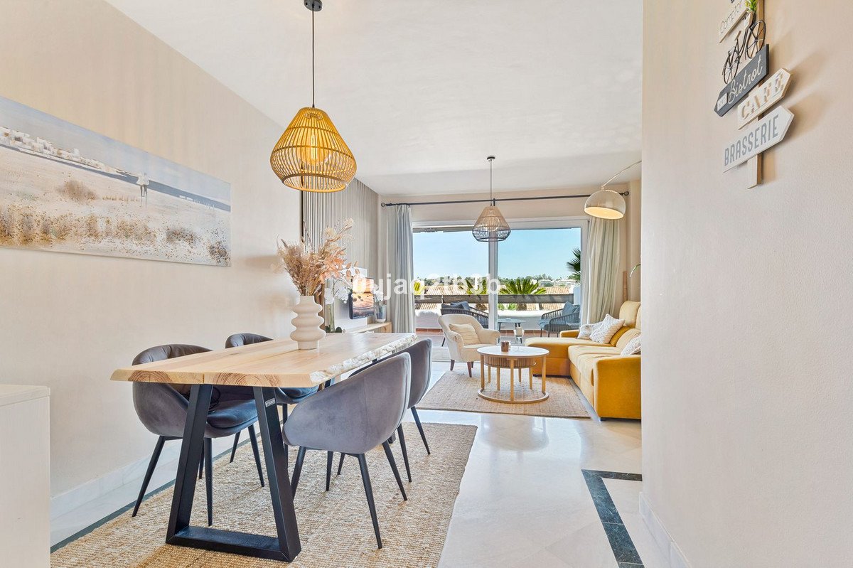 Modern dining and living area with large windows offering a view of palm trees and rooftops.