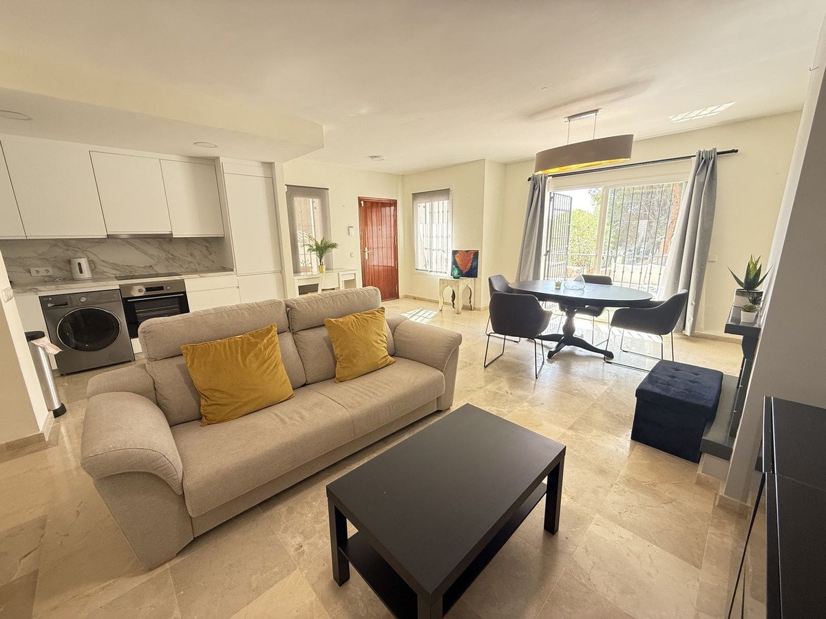 Modern open-plan living, dining, and kitchen area with a sofa, dining table, and access to an outdoor view.