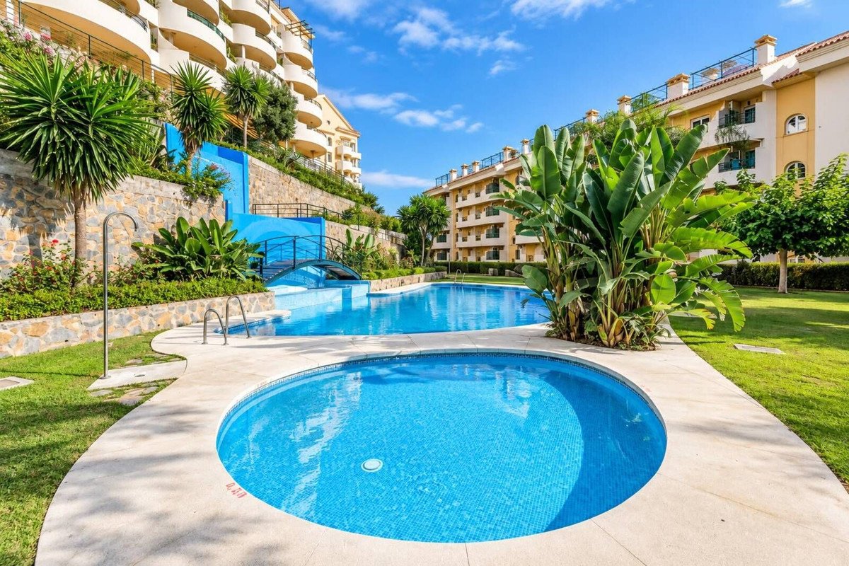 Outdoor swimming pool area with a jacuzzi, surrounded by lush greenery and apartment buildings under a clear blue sky.