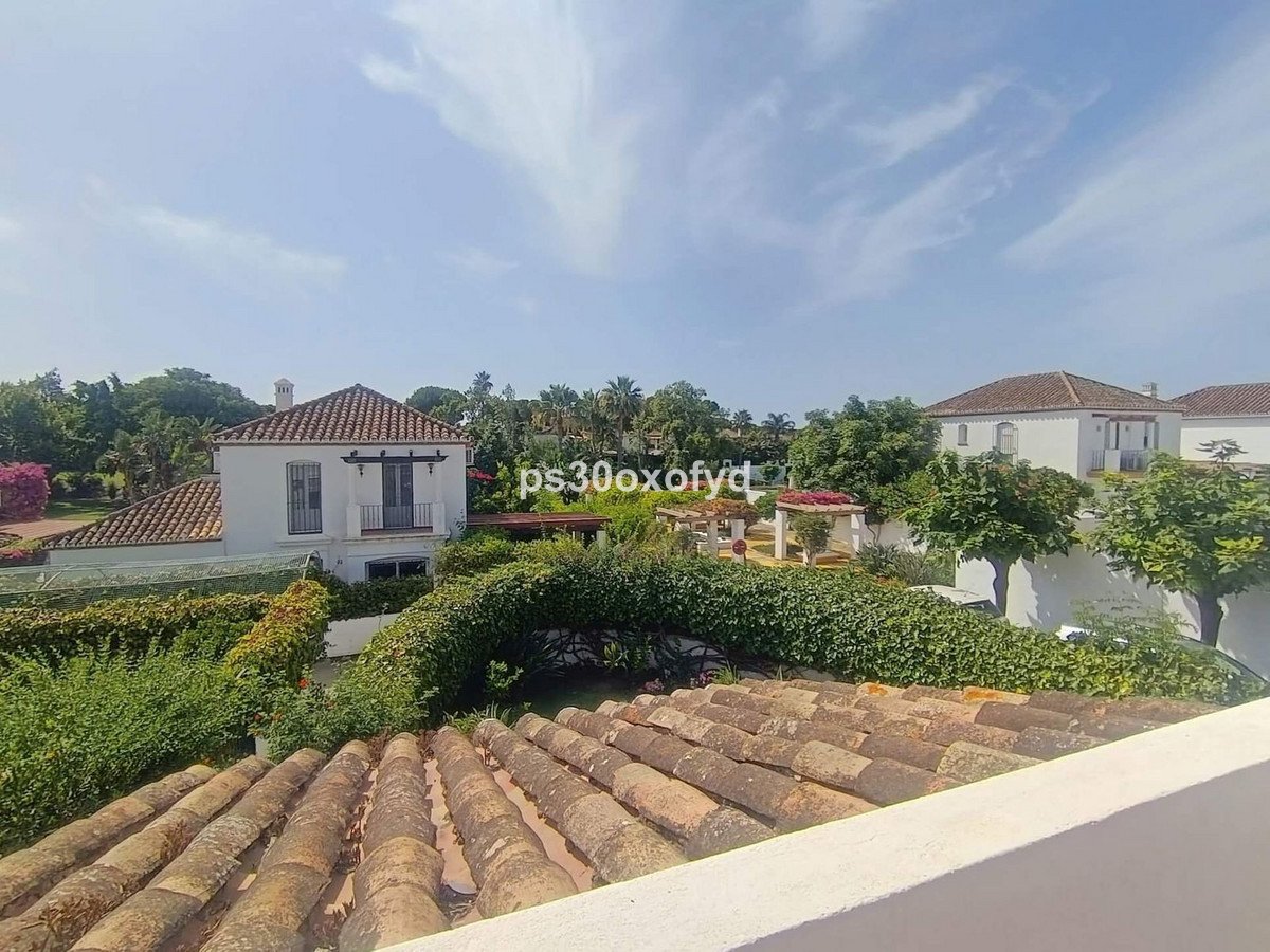 Spanish villa with a lush garden and tiled roof, overlooking trees and a blue sky.