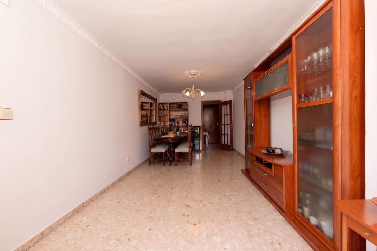 Living and dining area with wooden furniture, a dining table with chairs, bookshelves, and a large display cabinet.