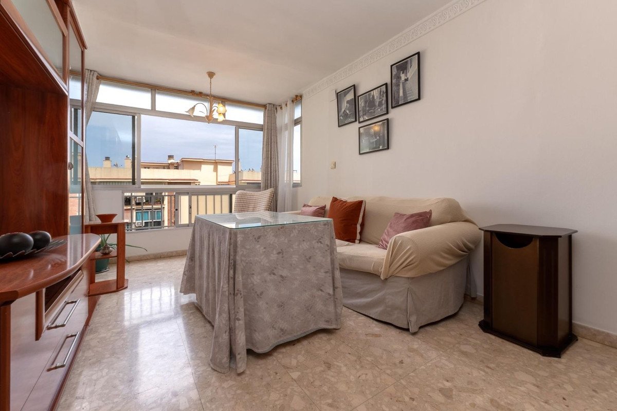Cozy living room with a sofa, a glass-top table, and large windows offering a view of the city buildings.