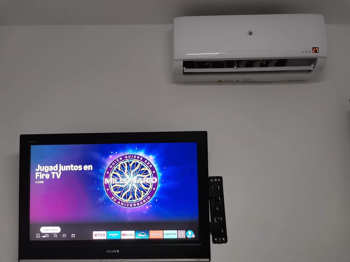 A television screen displaying a game show menu, with a wall-mounted air conditioner above it.