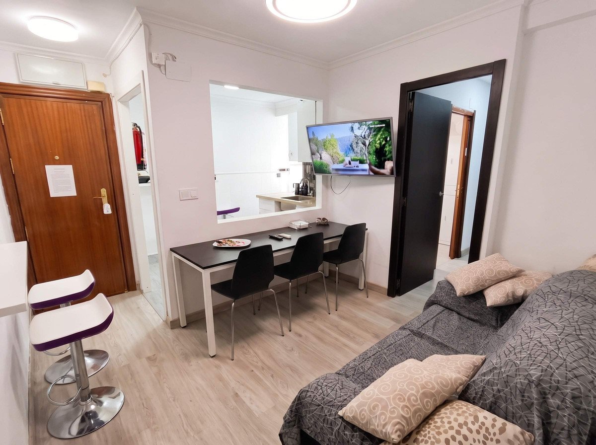 Studio apartment with dining table for three, sofa, and kitchen view through pass-through.