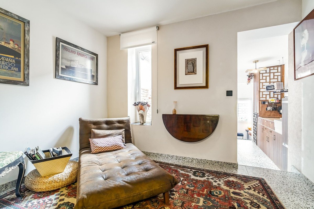 A brown chaise lounge with pillows in a room featuring vintage posters and artwork on the walls.