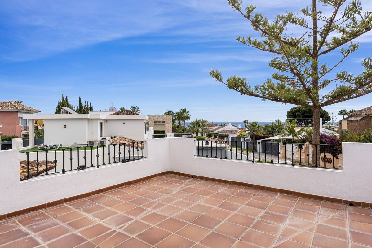 Terrace with tiled floor, black railings, and ocean view, featuring a tree and surrounding houses.
