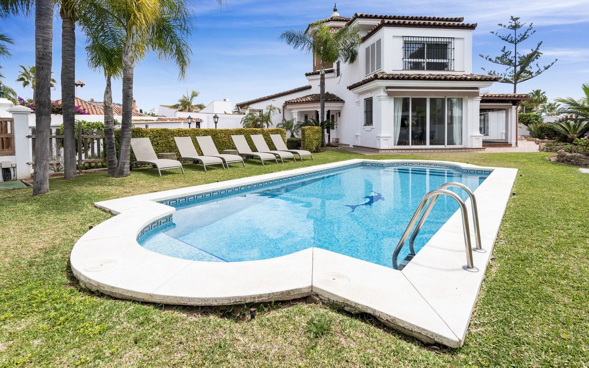 Luxurious swimming pool with lounge chairs and a modern two-story house in the background