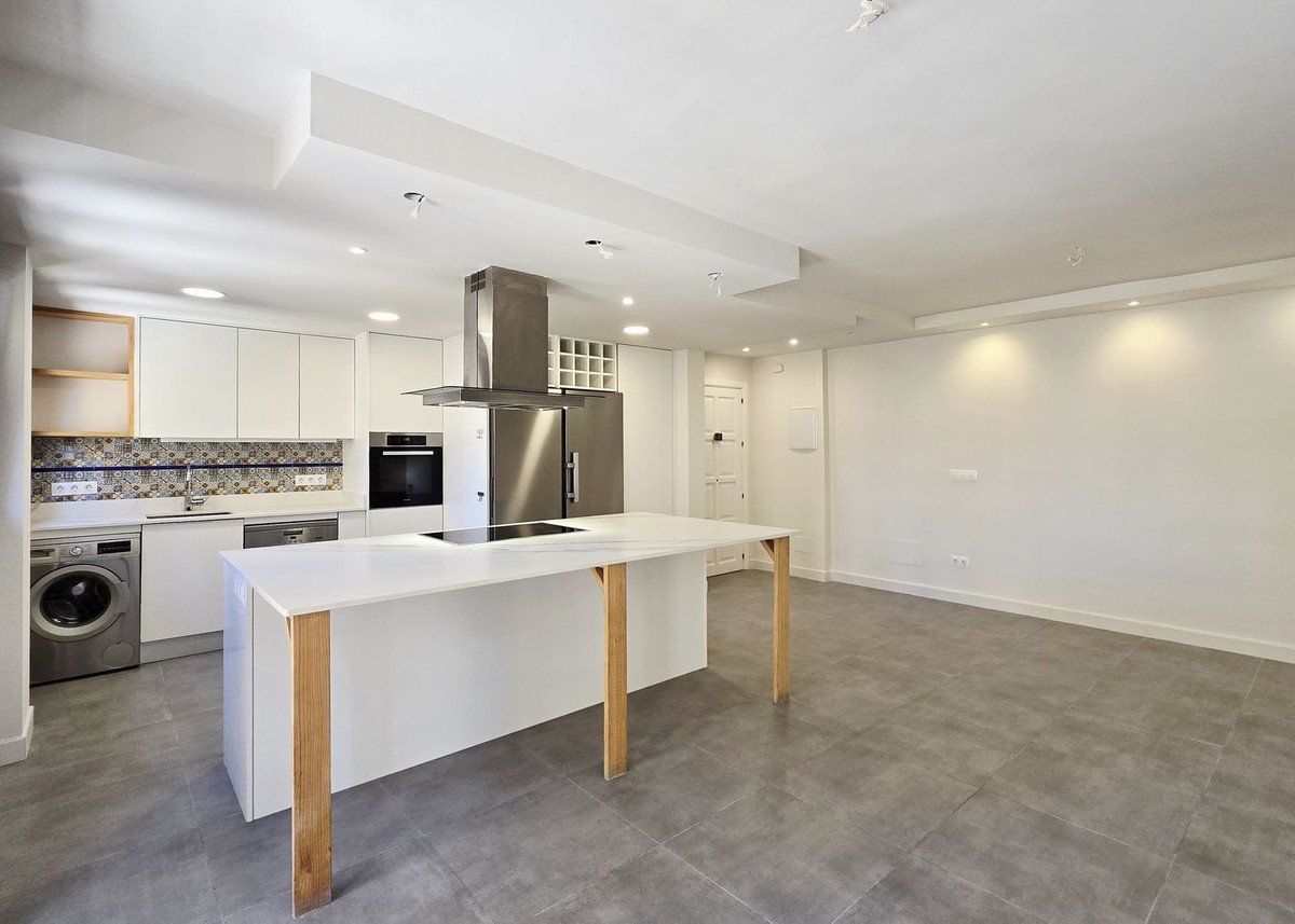 A modern, open-plan kitchen featuring a central island with a stovetop, sleek white cabinetry, and stainless steel appliances.