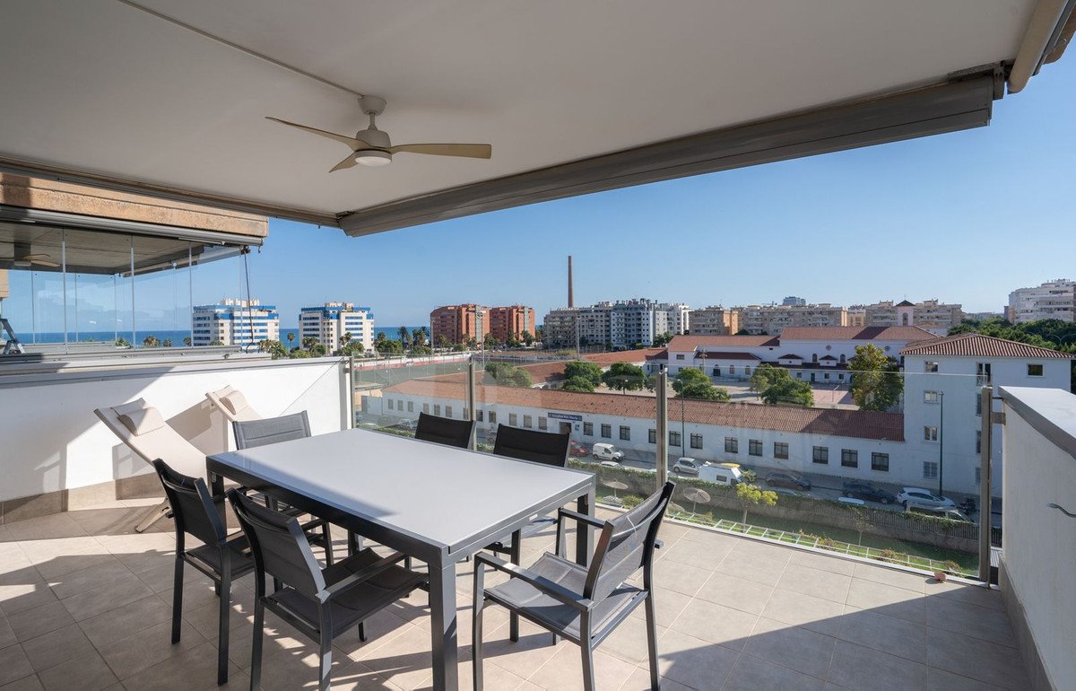 Spacious balcony with sea view, dining table, chairs, and lounge chair. Overlooking city buildings and the ocean.