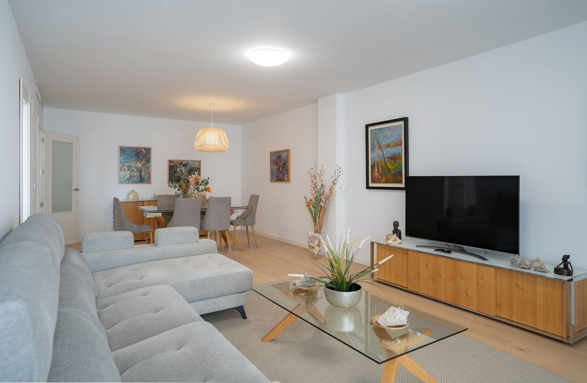 A modern living and dining area with a sectional sofa, glass coffee table, dining set, and a large TV mounted above a credenza.